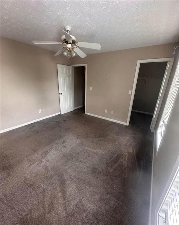 unfurnished room with a textured ceiling, dark carpet, a ceiling fan, and baseboards