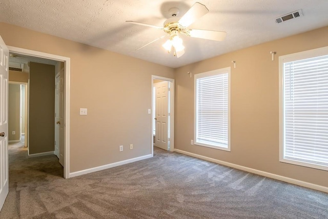 unfurnished room with a textured ceiling, carpet floors, a ceiling fan, visible vents, and baseboards