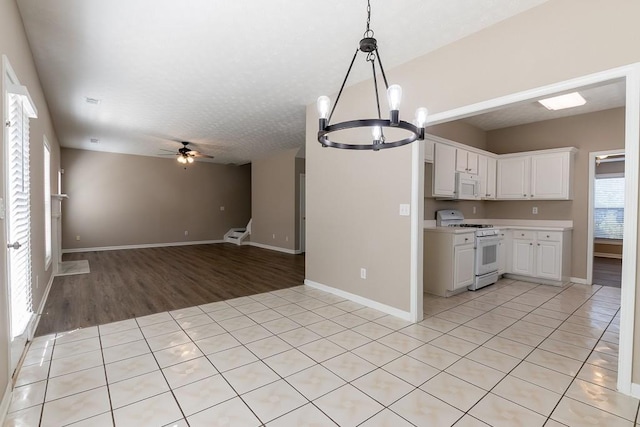 kitchen featuring white appliances, white cabinets, open floor plan, light countertops, and ceiling fan with notable chandelier