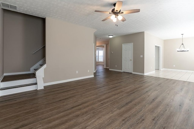 unfurnished living room with dark wood finished floors, visible vents, stairway, a textured ceiling, and ceiling fan with notable chandelier