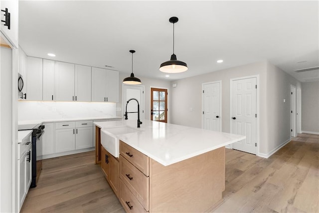 kitchen featuring a large island, sink, white cabinets, black range, and decorative light fixtures