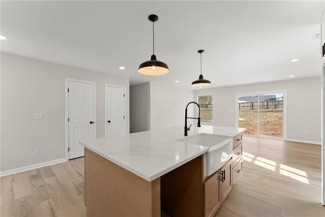 kitchen featuring sink, hanging light fixtures, a center island with sink, light stone countertops, and light hardwood / wood-style floors