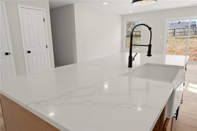 interior details featuring light stone countertops, sink, a kitchen island with sink, and light hardwood / wood-style floors