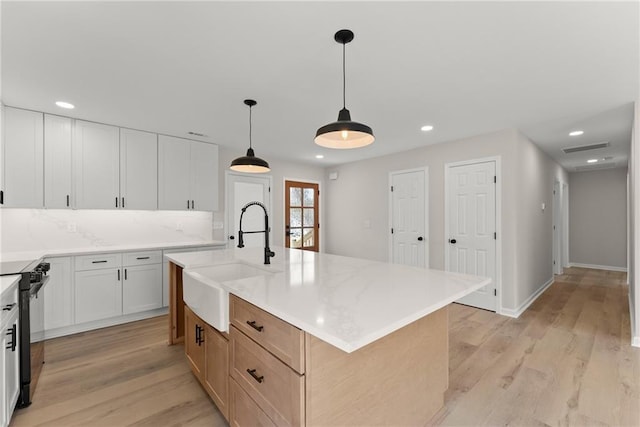 kitchen featuring sink, stove, white cabinets, a center island with sink, and decorative light fixtures