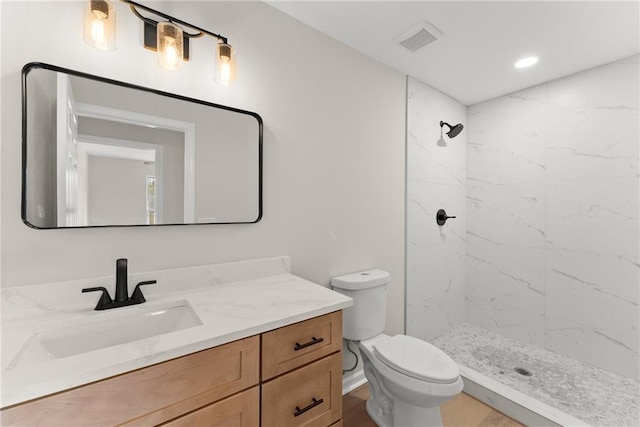 bathroom featuring vanity, a tile shower, and toilet