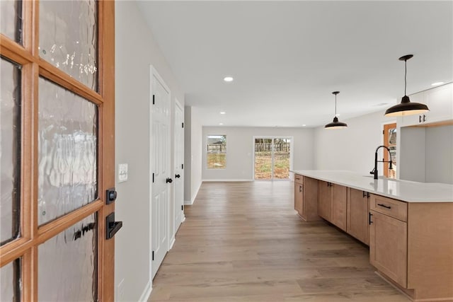 kitchen featuring sink, light brown cabinets, hanging light fixtures, light hardwood / wood-style floors, and a center island with sink