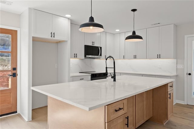 kitchen featuring white cabinetry, pendant lighting, a center island with sink, and light stone counters