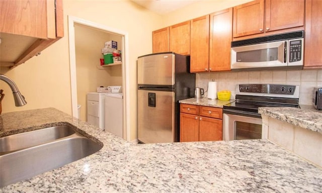 kitchen with sink, washer and clothes dryer, backsplash, stainless steel appliances, and light stone countertops