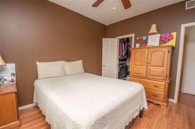 bedroom featuring a walk in closet, a closet, ceiling fan, and light wood-type flooring