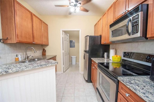 kitchen with stainless steel appliances, light tile patterned flooring, light stone countertops, and sink