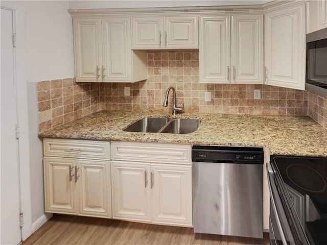 kitchen with sink, stainless steel appliances, light stone counters, light hardwood / wood-style flooring, and decorative backsplash