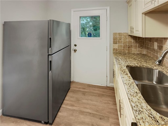 kitchen with sink, light wood-type flooring, tasteful backsplash, light stone counters, and stainless steel refrigerator