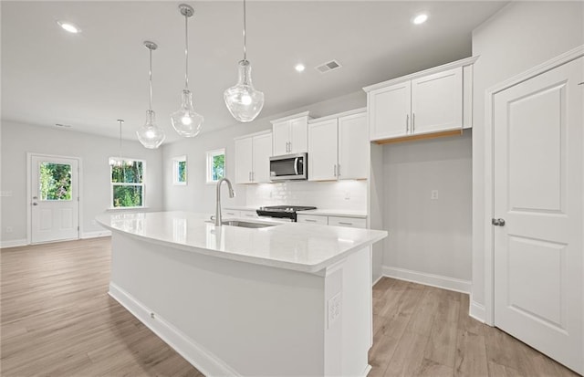 kitchen featuring sink, hanging light fixtures, a kitchen island with sink, appliances with stainless steel finishes, and white cabinets