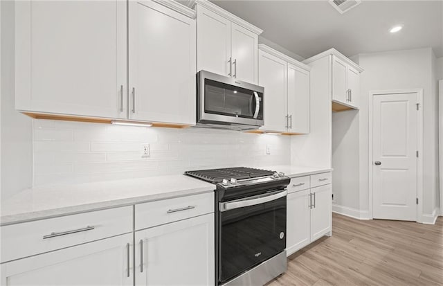 kitchen featuring light hardwood / wood-style floors, backsplash, stainless steel appliances, and white cabinetry