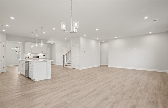 kitchen with white cabinets, light hardwood / wood-style flooring, hanging light fixtures, and an island with sink