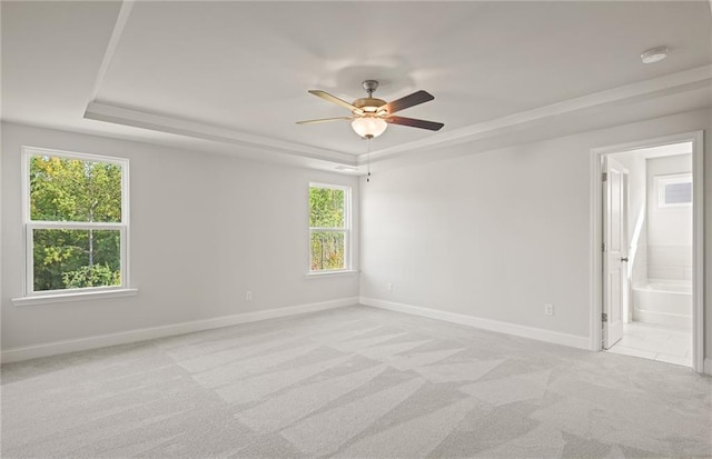 spare room with ceiling fan, light colored carpet, and a tray ceiling