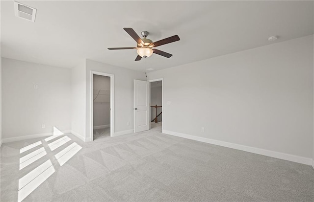 unfurnished bedroom featuring ceiling fan, a walk in closet, a closet, and light colored carpet