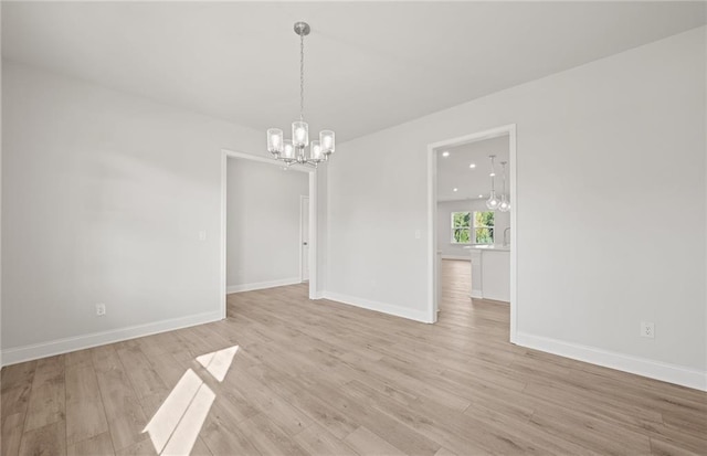 spare room with light hardwood / wood-style floors and an inviting chandelier