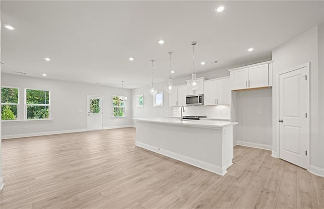 kitchen with light hardwood / wood-style flooring, white cabinets, a center island with sink, and hanging light fixtures