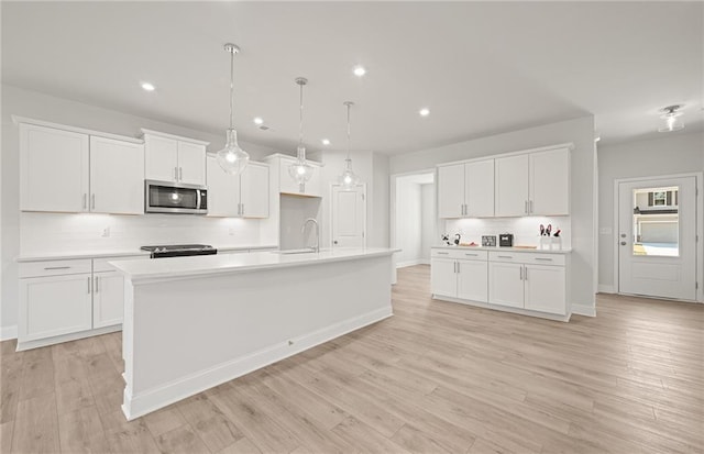 kitchen featuring tasteful backsplash, white cabinets, an island with sink, and pendant lighting