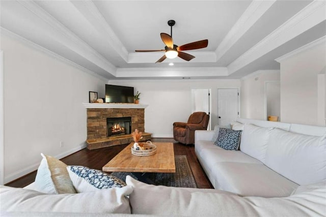 living room featuring dark wood-type flooring, crown molding, a raised ceiling, a fireplace, and ceiling fan