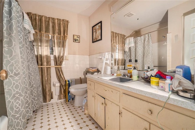 bathroom featuring walk in shower, toilet, vanity, and tile walls