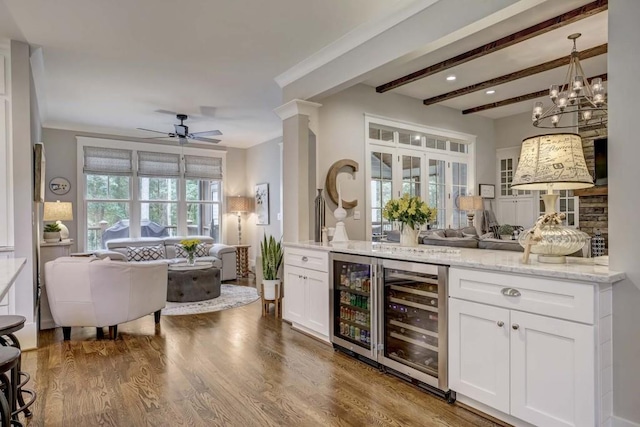 bar featuring white cabinetry, beverage cooler, light stone counters, decorative light fixtures, and hardwood / wood-style flooring