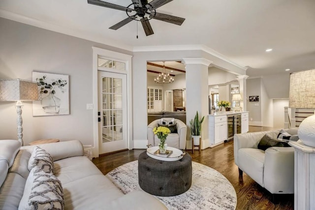 living room featuring decorative columns, ornamental molding, ceiling fan with notable chandelier, dark hardwood / wood-style floors, and wine cooler