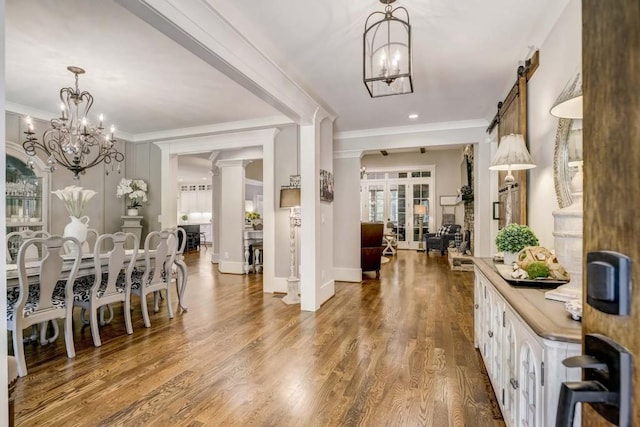 corridor with ornate columns, french doors, a barn door, crown molding, and hardwood / wood-style floors