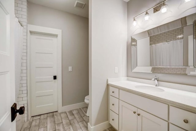 bathroom with hardwood / wood-style floors, vanity, toilet, and walk in shower