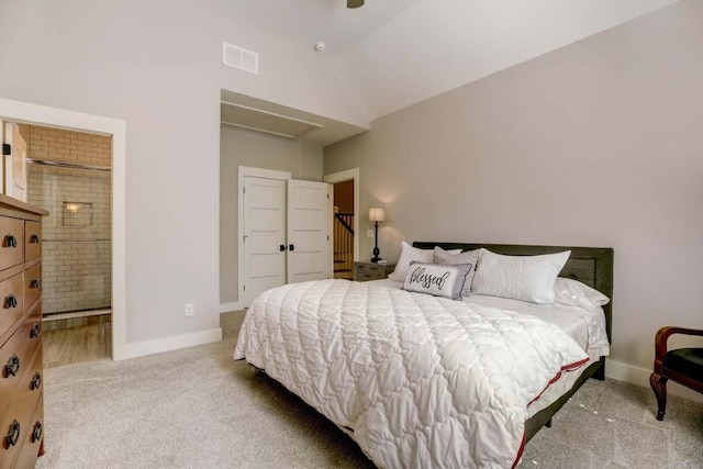 bedroom with lofted ceiling, light carpet, and ensuite bath