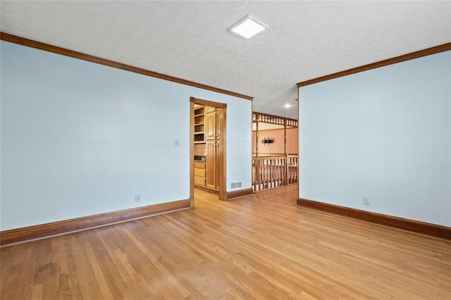 empty room with ornamental molding, visible vents, light wood-style flooring, and baseboards