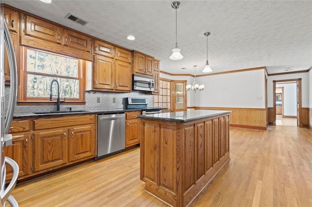 kitchen featuring a sink, visible vents, appliances with stainless steel finishes, wainscoting, and brown cabinets