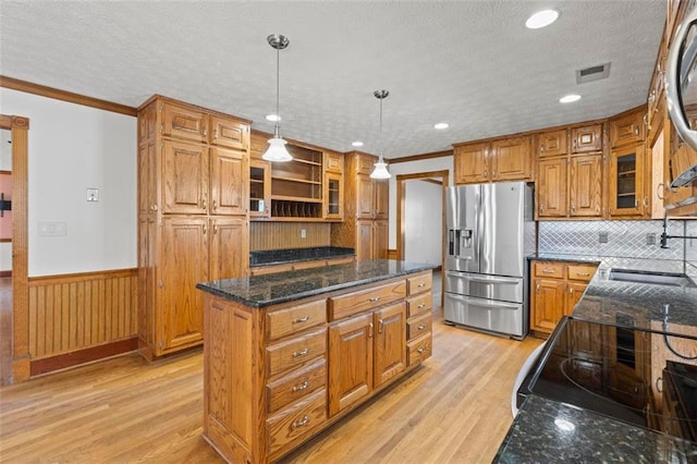 kitchen with a wainscoted wall, a sink, stainless steel fridge with ice dispenser, a center island, and brown cabinetry