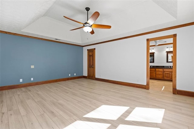 spare room featuring light wood-type flooring, a raised ceiling, visible vents, and baseboards