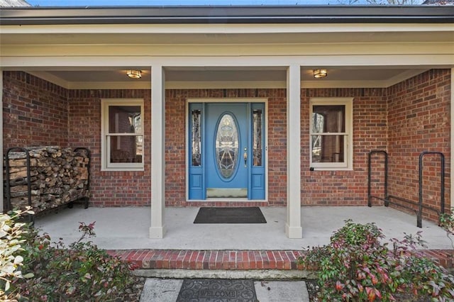 entrance to property featuring a porch and brick siding