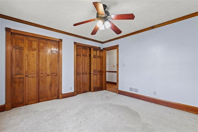 unfurnished bedroom featuring carpet floors, visible vents, crown molding, and baseboards