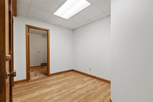 empty room featuring a baseboard heating unit, a drop ceiling, light wood-style flooring, and baseboards