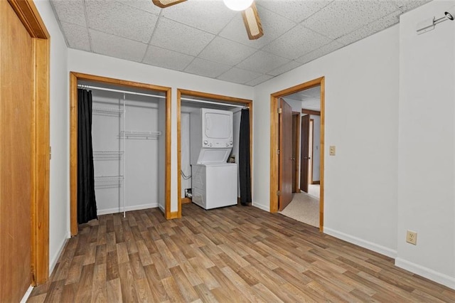 unfurnished bedroom with light wood-type flooring, baseboards, a drop ceiling, and stacked washing maching and dryer