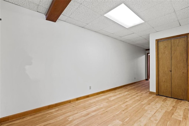 basement featuring baseboards, a drop ceiling, and light wood-style floors