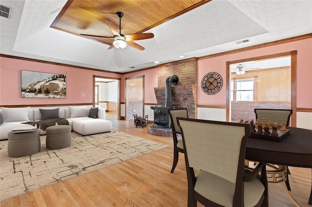 living area with a wood stove, wood finished floors, a raised ceiling, and visible vents