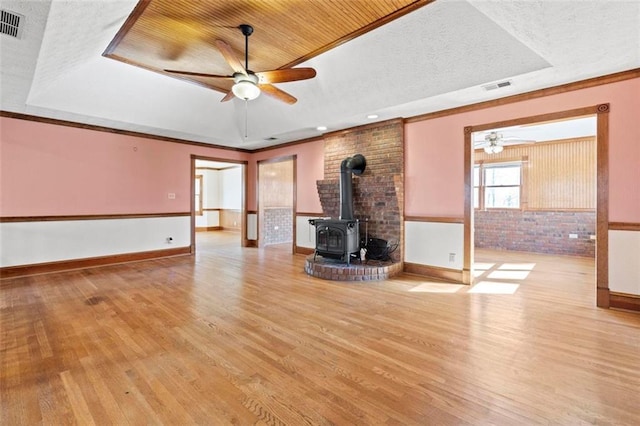 unfurnished living room with visible vents, a tray ceiling, wood finished floors, and a wood stove