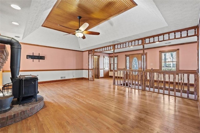 living area with a raised ceiling, a wood stove, a textured ceiling, wood finished floors, and baseboards