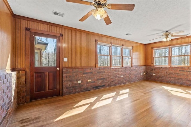 entryway with brick wall, a textured ceiling, visible vents, and wood finished floors