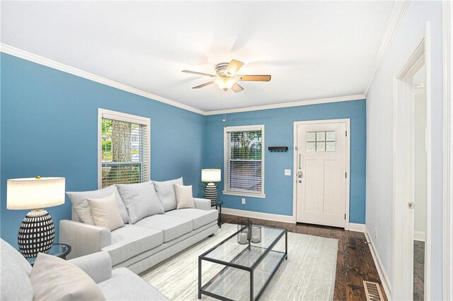 living room with wood finished floors, ornamental molding, baseboards, visible vents, and a ceiling fan