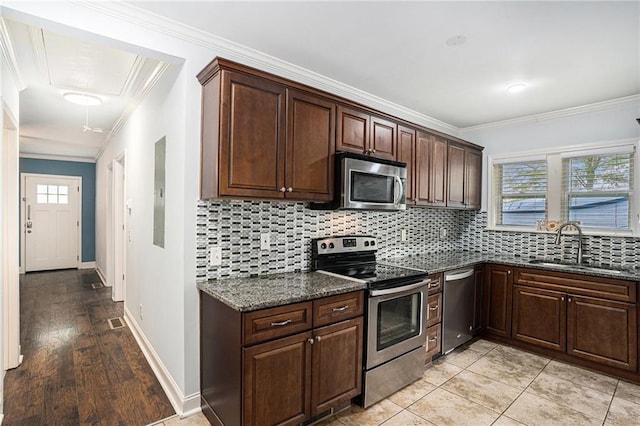 kitchen featuring dark stone counters, tasteful backsplash, a sink, appliances with stainless steel finishes, and ornamental molding