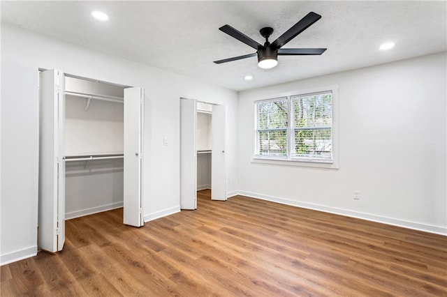 unfurnished bedroom with two closets, wood finished floors, recessed lighting, baseboards, and ceiling fan