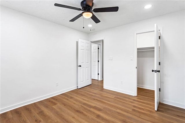 unfurnished bedroom featuring ceiling fan, a walk in closet, baseboards, and wood finished floors