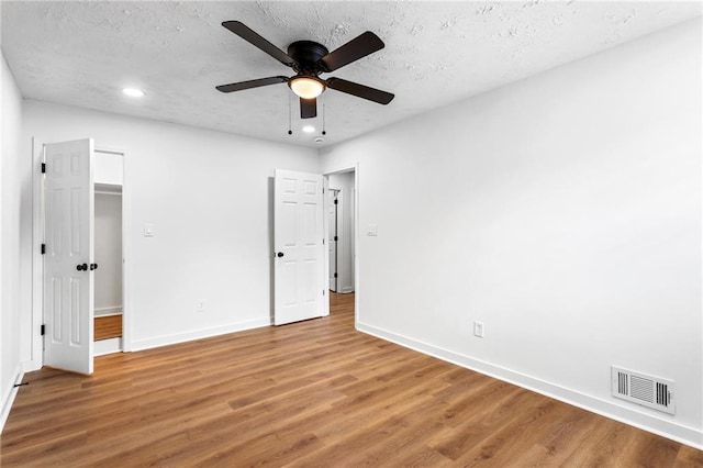 unfurnished bedroom featuring visible vents, a textured ceiling, baseboards, and wood finished floors