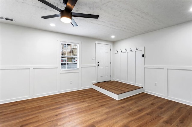 interior space with ceiling fan, visible vents, wood finished floors, and a decorative wall